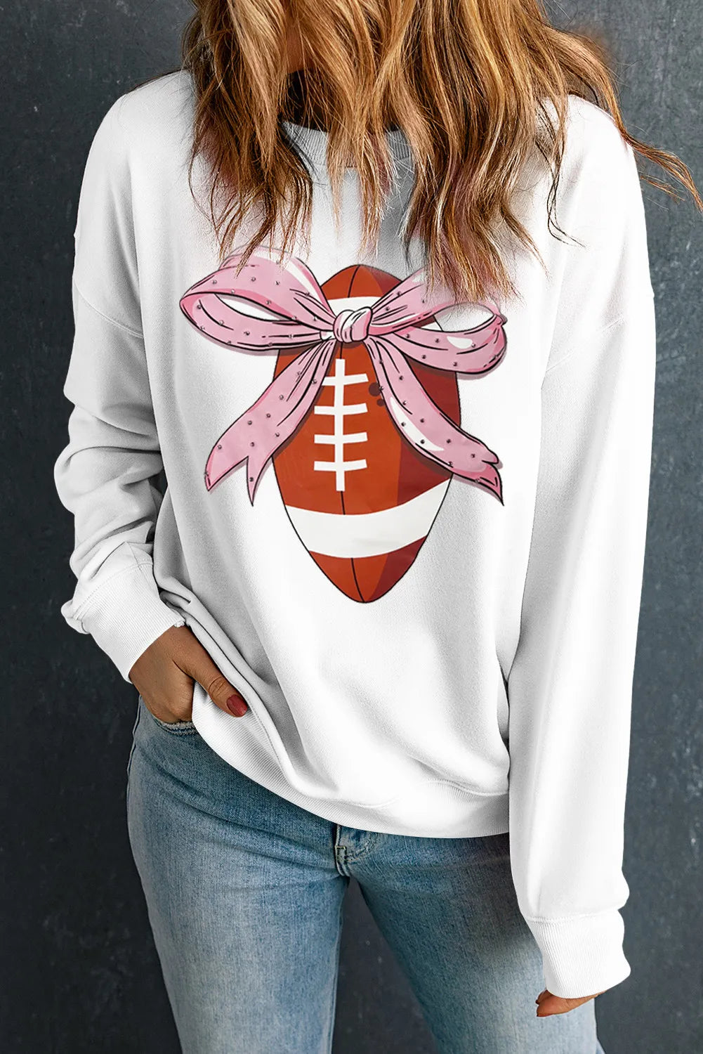 White sweatshirt with football graphic and pink polka dot bow detail.