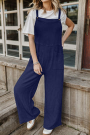 Dark blue textured cotton overalls with square pockets and button straps, worn with a white tee.