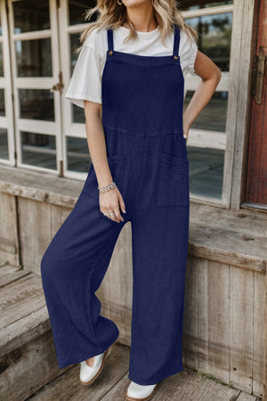 Dark blue textured cotton overalls with square pockets and button straps, worn with a white tee.