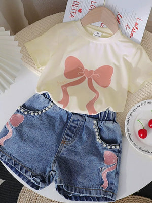 Beige tee with pink bowknot graphic and pearl-trimmed denim shorts with pink bowknot detail.