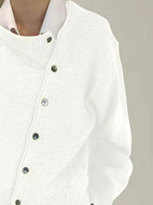 White asymmetric button-up knit cardigan with dark buttons, styled over a collared shirt.