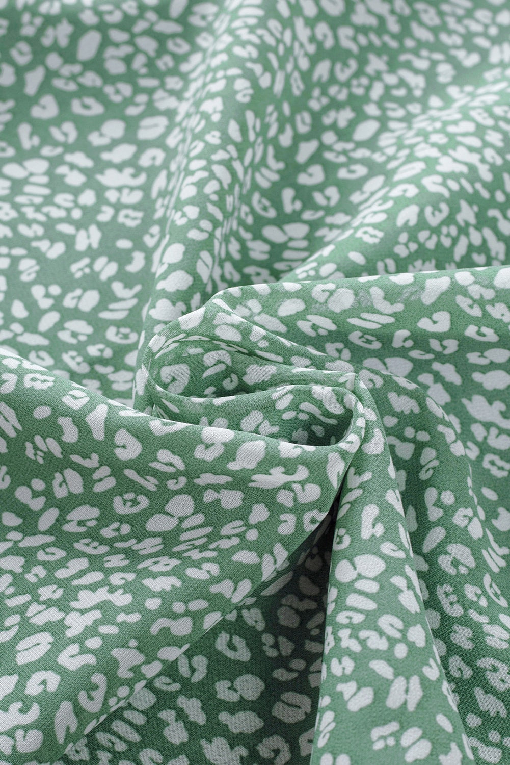 Sleeveless sage green blouse with white abstract print and ruffled neckline detail.