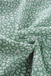 Sleeveless sage green blouse with white abstract print and ruffled neckline detail.