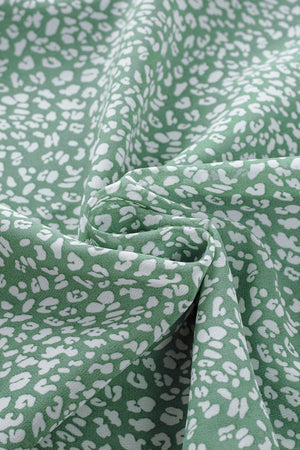 Sleeveless sage green blouse with white abstract print and ruffled neckline detail.