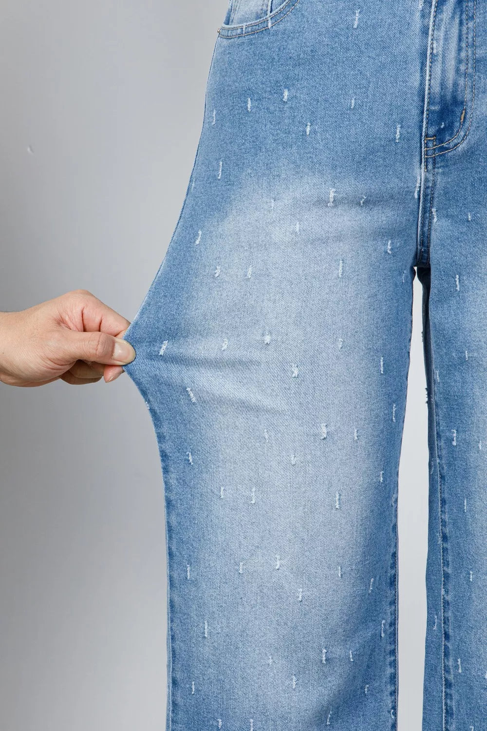 Light wash denim jeans with allover distressed details and a raw hem.