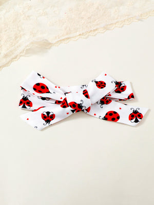 White baby headband with red ladybug print and bow detail