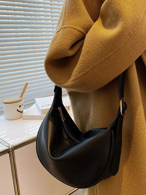 Black minimalist crescent crossbody bag with adjustable strap and gold hardware detail.