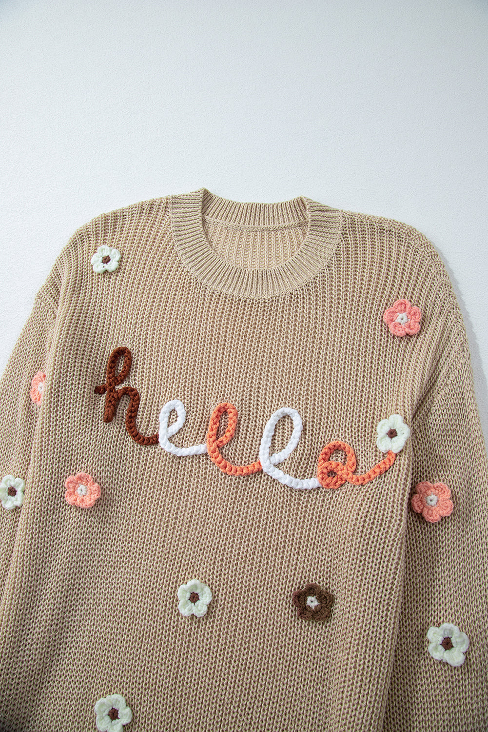 Khaki knit sweater with embroidered "hello" and floral appliques.