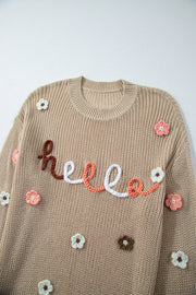 Khaki knit sweater with embroidered "hello" and floral appliques.