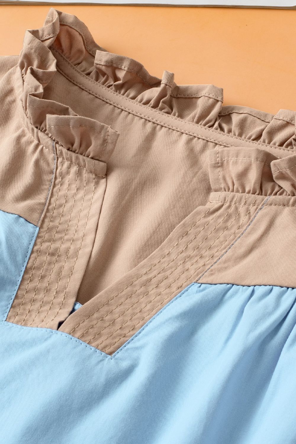 Colorblock ruffle yoke blouse in tan and light blue with decorative stitching.