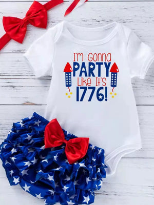 White patriotic baby onesie with red and blue text and ruffled bloomer with stars and red bow.