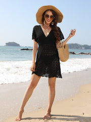 Black openwork knit beach mini dress with V-neck and short sleeves, styled with a straw hat and bag.