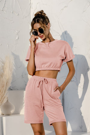 Blush pink loungewear set with rolled sleeve crop top and drawstring shorts.