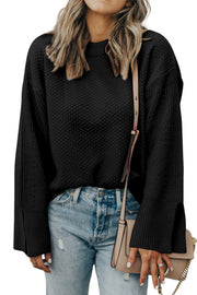 Black textured knit sweater with crewneck and slit sleeves, styled with jeans.