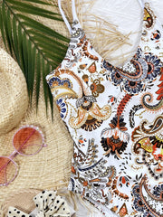 White paisley print one-piece swimsuit with white straps and a tie-back detail.